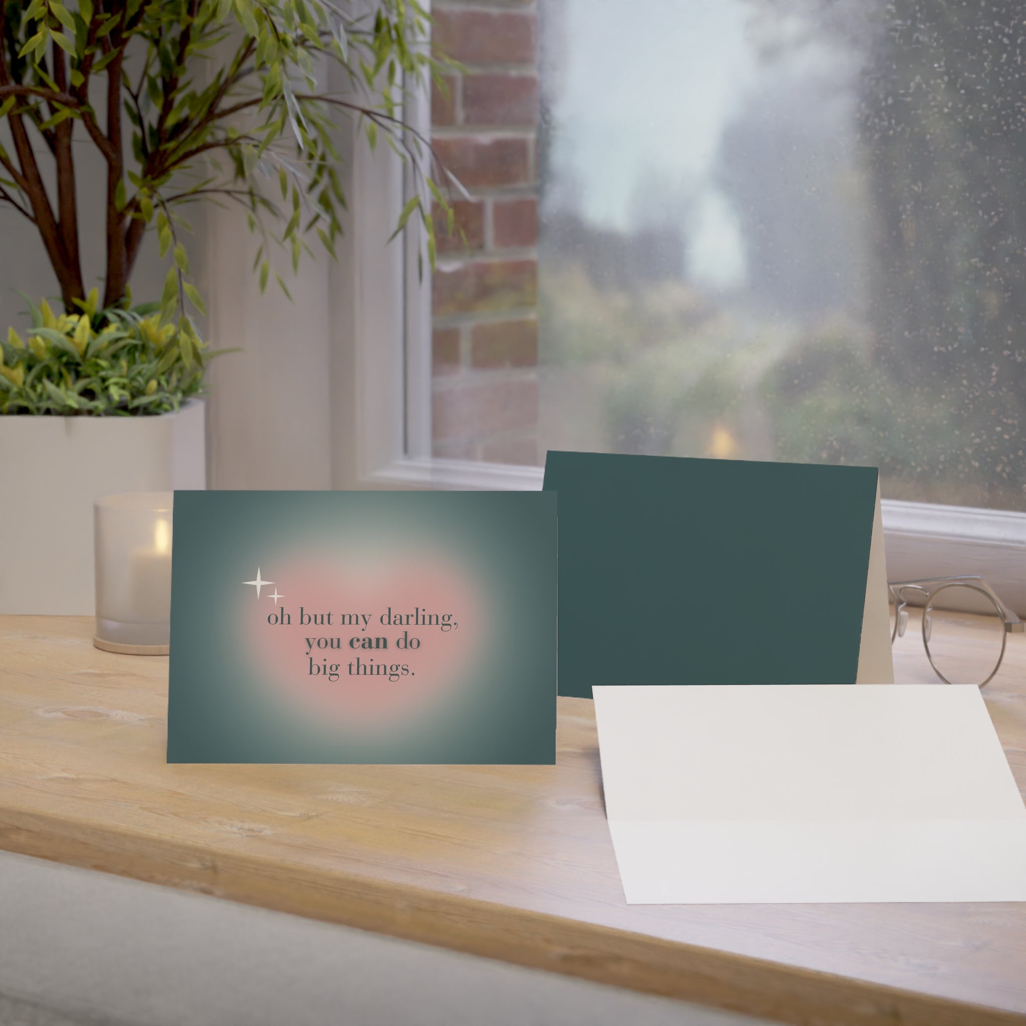 Greeting cards on a wooden surface with a plant and candle in the background